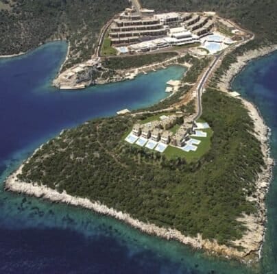 Berrak mavi sularla çevrili yemyeşil bir yarımada üzerine inşa edilmiş bir kıyı tatil beldesinin havadan görünümü. Tatil beldesinde beyaz çatılı, teraslı yerleşimli ve yüzme havuzlu çok sayıda bina bulunmaktadır. Yarımadanın çoğunu kaplayan kayalık kıyılar ve yoğun yeşillikler vardır. Berrak mavi sularla çevrili yemyeşil bir yarımada üzerine inşa edilmiş bir kıyı tatil beldesinin havadan görünümü. Tatil beldesinde beyaz çatılı, teraslı yerleşimli ve yüzme havuzlu çok sayıda bina bulunmaktadır. Yarımadanın çoğunu kaplayan kayalık kıyılar ve yoğun yeşillikler vardır.