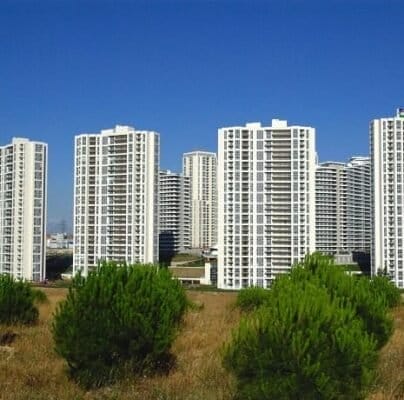 Çok sayıda balkonu olan uzun, beyaz konut apartman binaları grubu, berrak, mavi bir gökyüzünün önünde duruyor. Ön planda, dağınık yeşil çalılarla çimenli bir alan yer alıyor ve kentsel manzaraya doğal bir kontrast sağlıyor. Binalar tasarım olarak tekdüze ve eşit aralıklarla yerleştirilmiş. Çok sayıda balkonu olan uzun, beyaz konut apartman binaları grubu, berrak, mavi bir gökyüzünün önünde duruyor. Ön planda, dağınık yeşil çalılarla çimenli bir alan yer alıyor ve kentsel manzaraya doğal bir kontrast sağlıyor. Binalar tasarım olarak tekdüze ve eşit aralıklarla yerleştirilmiş.