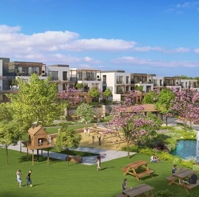 A lush community park in BIRLESIM with modern multi-story buildings in the background. The park features a playground with children playing, a pond with fountains, blossoming trees, and well-maintained lawns. People are walking, sitting on benches, and enjoying the serene environment under a blue sky with scattered clouds.