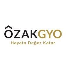 Türkçe metinli bir logo. Metinde büyük harflerle "ÖZAK GYO" yazıyor, siyah renkte "ÖZAK" ve altın renkte "GYO" yazıyor. Altta, daha küçük altın renkli metinde "Hayata Değer Katar" yazıyor, bu da "Hayata Değer Katar" anlamına geliyor ve "Yaşama Değer Katıyor" anlamına geliyor. Genel tasarım, beyaz bir arka planla minimalist.