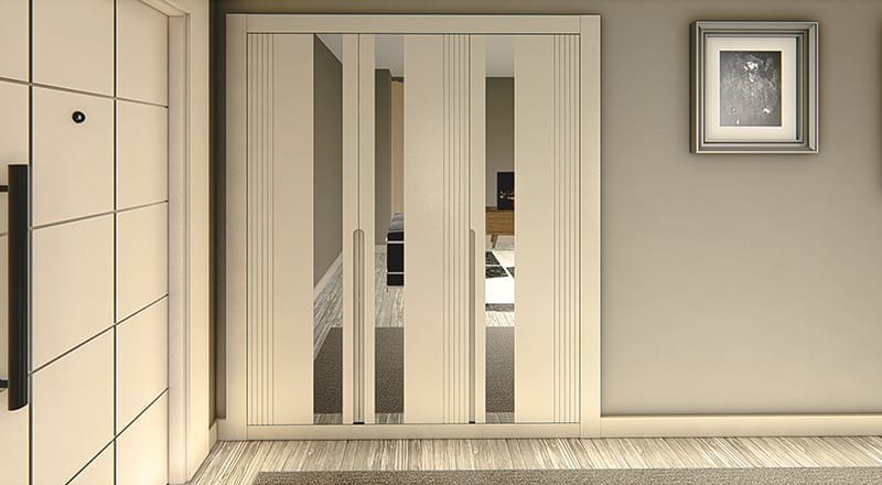 A modern interior features a beige double-door wardrobe with mirrored panels, positioned next to an entrance door. The wardrobe reflects part of a living room with a TV and wooden cabinet. On the wall to the right hangs a framed black-and-white picture. The flooring is a mix of tiles and rugs, seamlessly blending different textures in harmony.